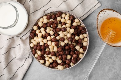 Photo of Tasty cereal balls in bowl, milk and honey on grey table, flat lay