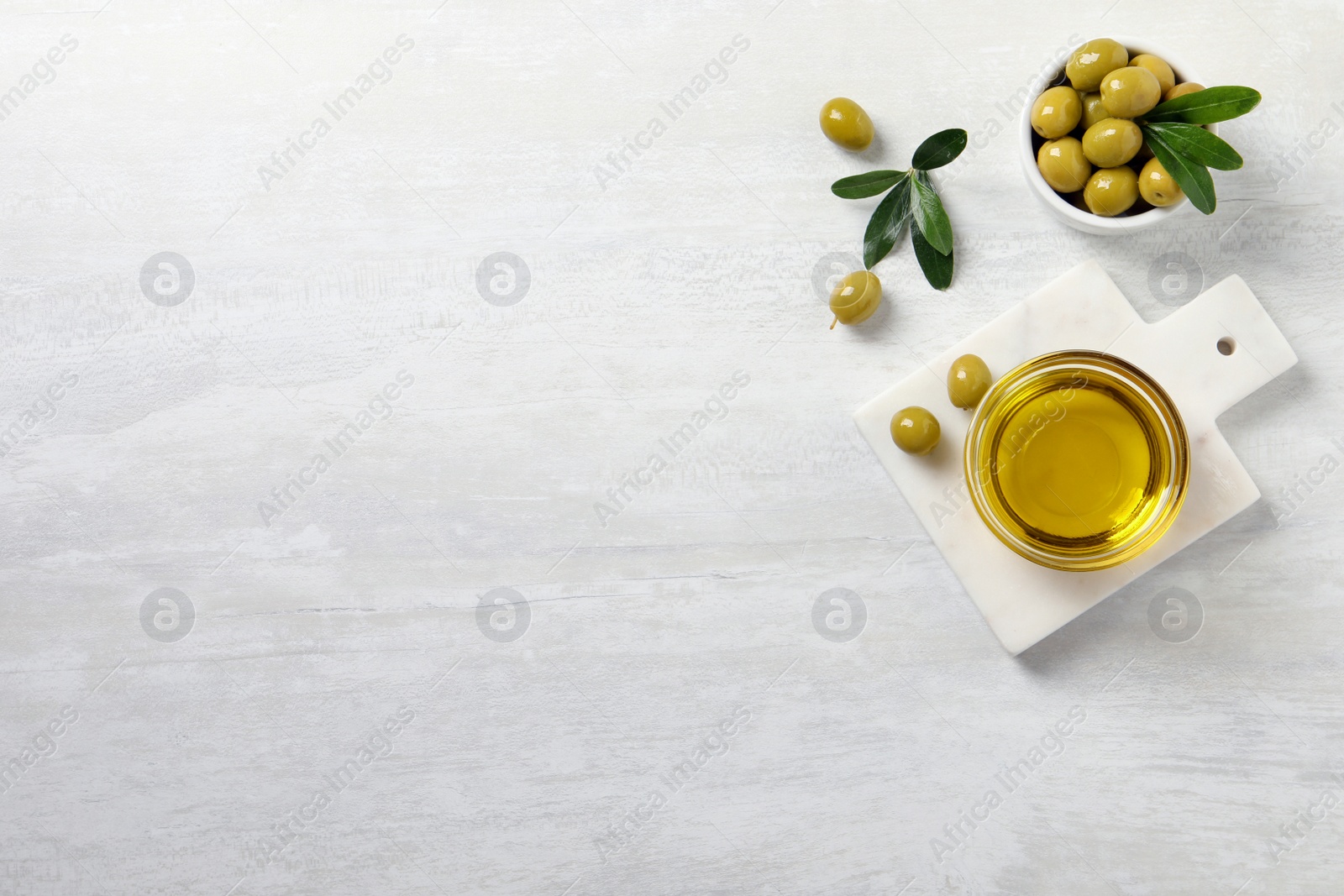 Photo of Glass bowl with fresh olive oil on white wooden table, flat lay. Space for text