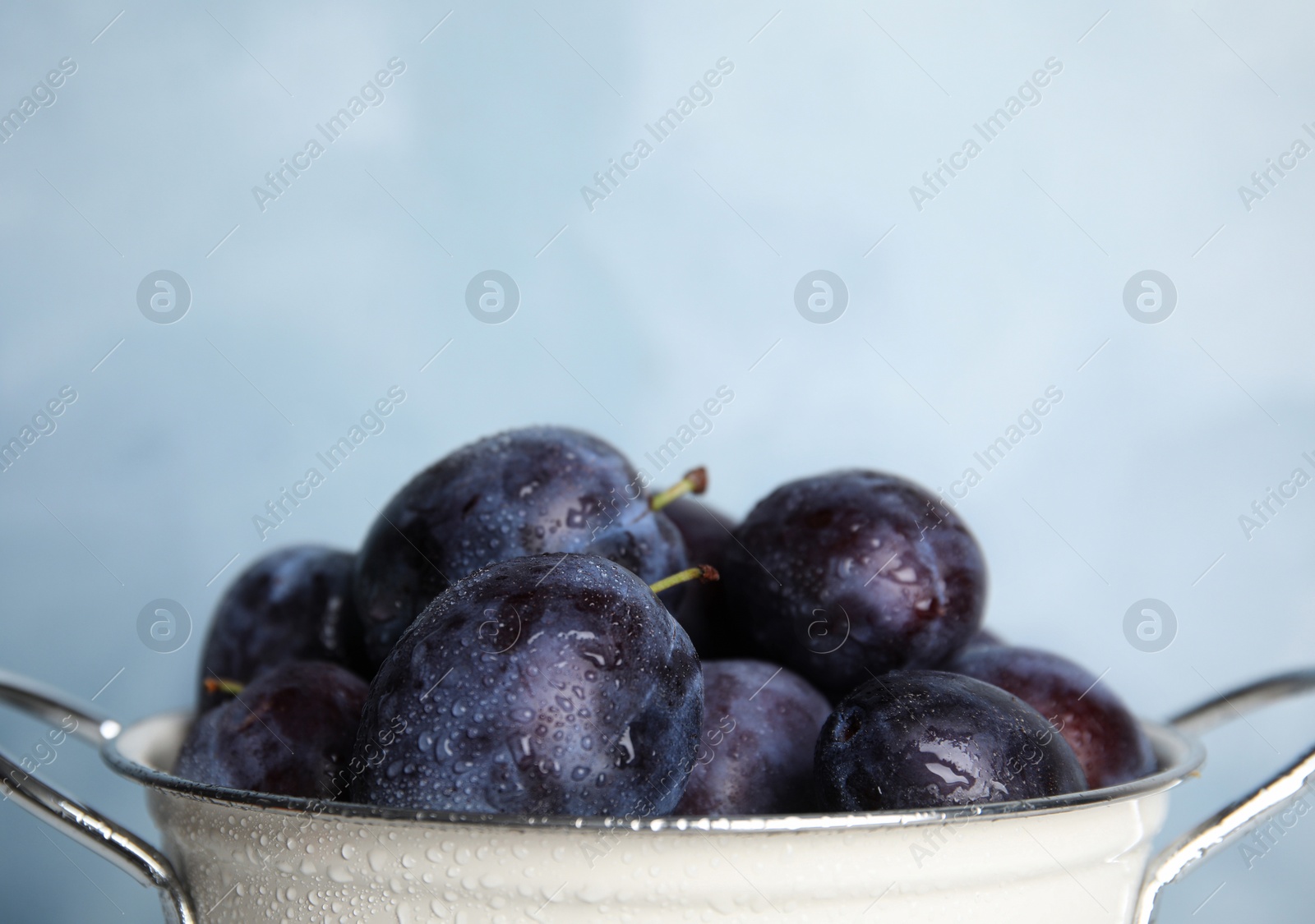 Photo of Delicious ripe plums in colander on light background, closeup. Space for text