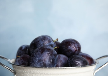 Delicious ripe plums in colander on light background, closeup. Space for text