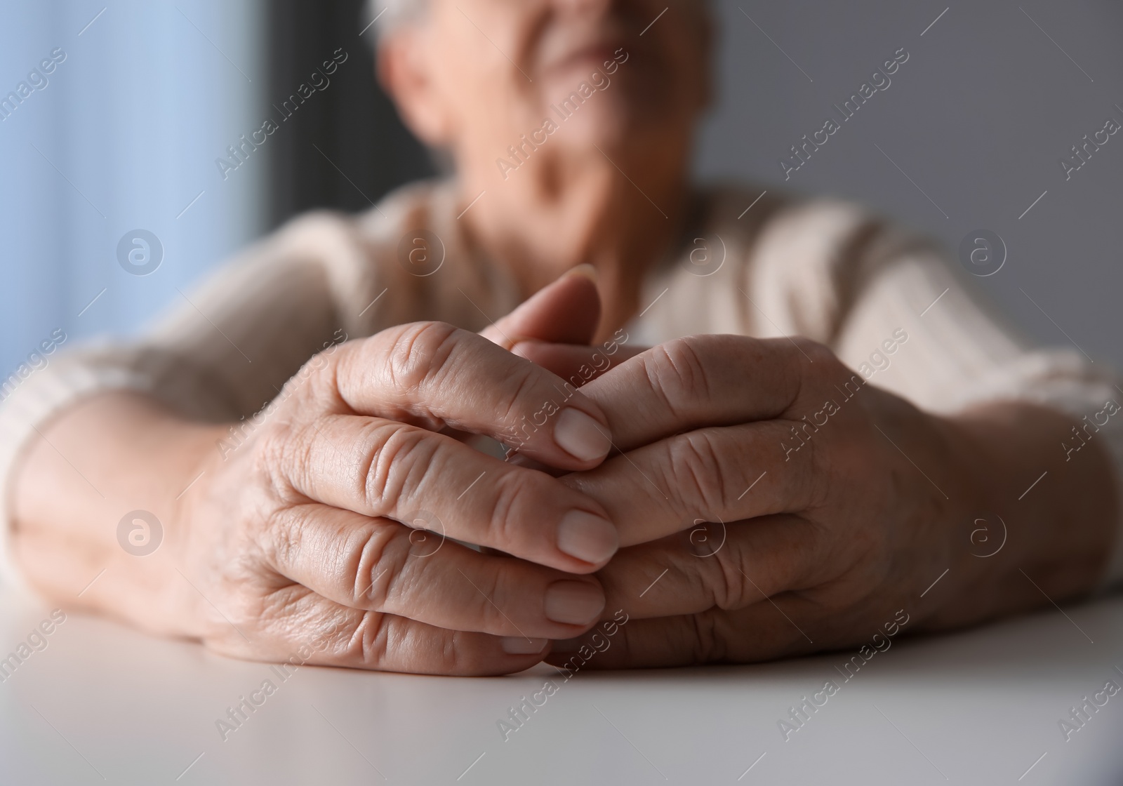 Photo of Elderly woman at white table indoors, closeup