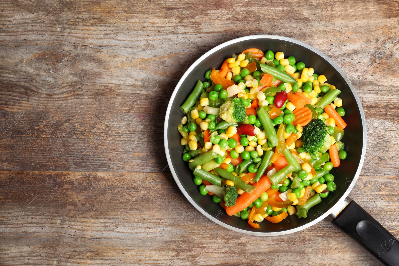 Photo of Frying pan with mix of frozen vegetables on wooden background, top view