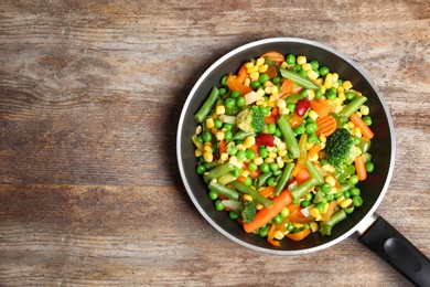 Photo of Frying pan with mix of frozen vegetables on wooden background, top view