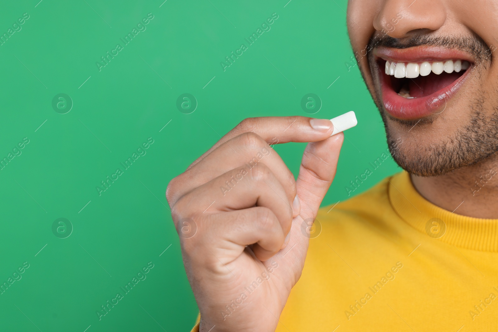 Photo of Happy man putting bubble gum into mouth on green background, closeup. Space for text