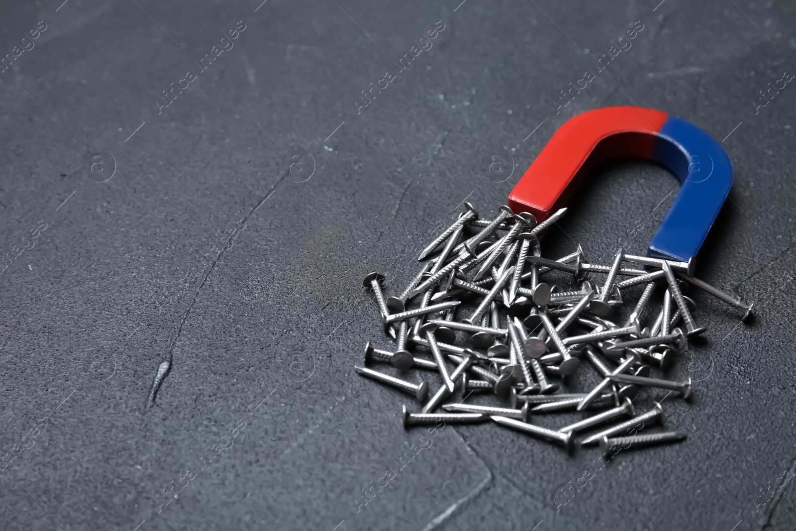 Photo of Magnet attracting nails on grey background, space for text