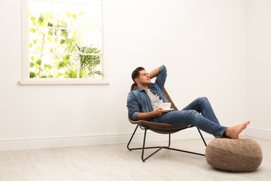 Attractive man relaxing in armchair near window at home. Space for text