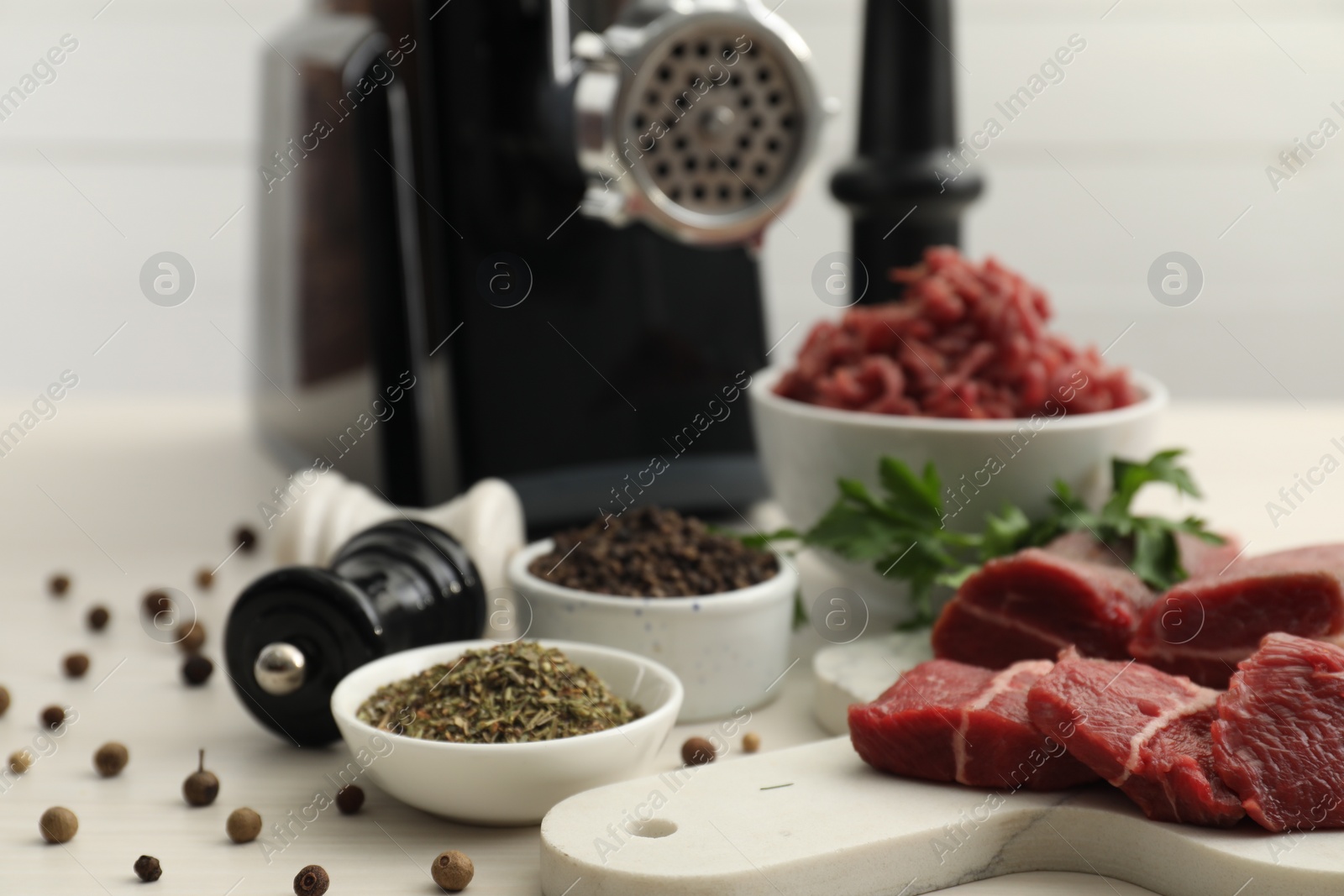 Photo of Meat grinder, beef, parsley and spices on white wooden table, closeup