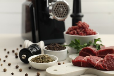 Photo of Meat grinder, beef, parsley and spices on white wooden table, closeup