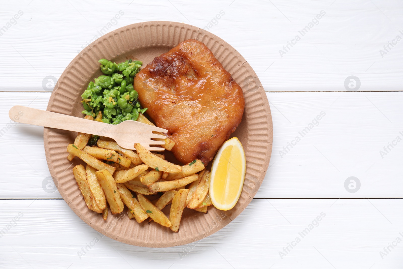 Photo of Tasty fish, chips, peas and lemon on white wooden table, top view. Space for text