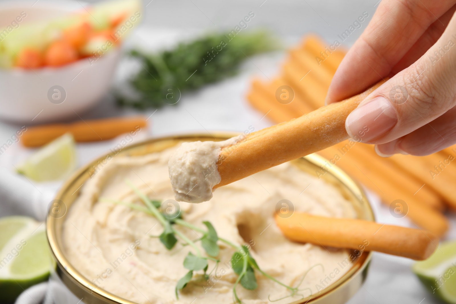 Photo of Woman dipping grissini stick into hummus at table, closeup