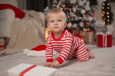 Photo of Cute baby in Christmas pajamas crawling on floor at home