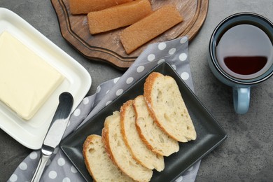Photo of Delicious quince paste, bread, butter and cup of tea on grey textured table, flat lay