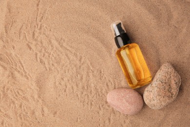 Bottle of serum and stones on sand, flat lay. Space for text