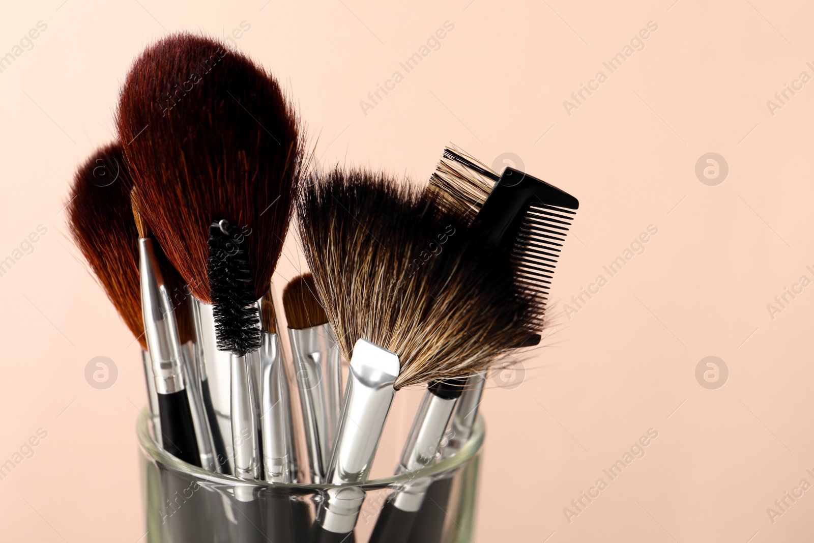 Photo of Set of professional makeup brushes against beige background, closeup