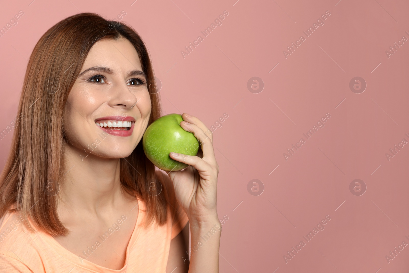 Photo of Smiling woman with perfect teeth and green apple on color background. Space for text