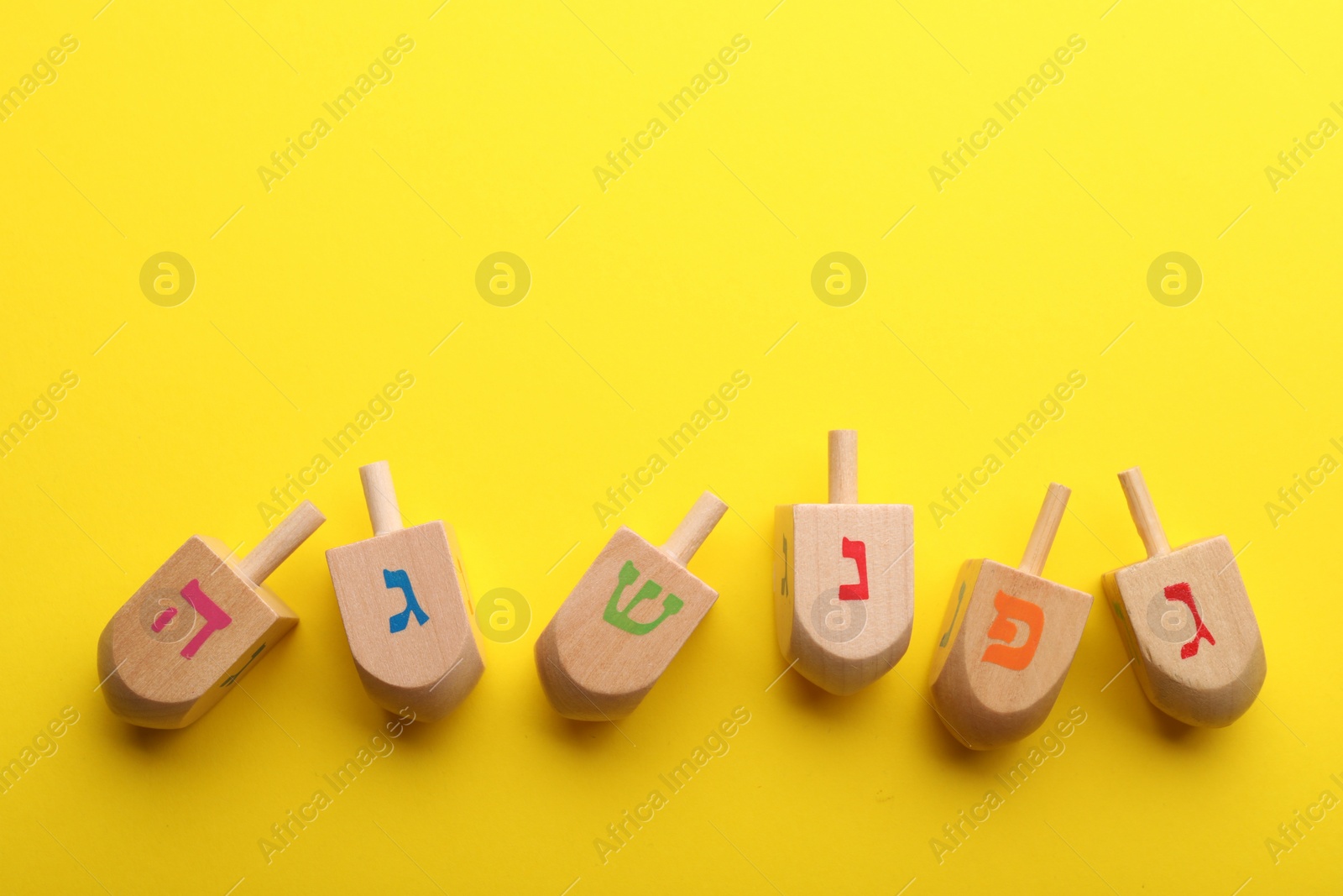 Photo of Wooden dreidels on yellow background, flat lay with space for text. Traditional Hanukkah game