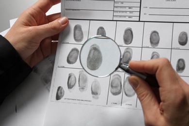 Female criminalist exploring fingerprints with magnifier at table, closeup