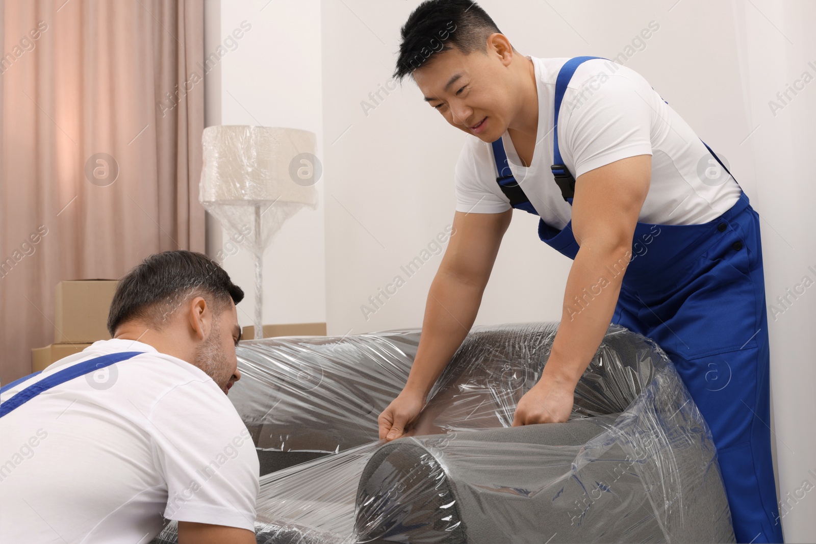 Photo of Workers wrapping sofa in stretch film indoors