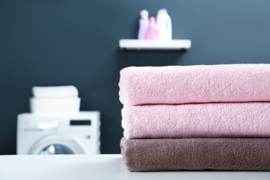 Stack of clean towels on table in laundry room, closeup. Space for text