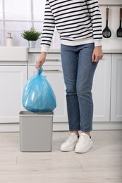 Photo of Woman taking garbage bag out of trash bin in kitchen, closeup