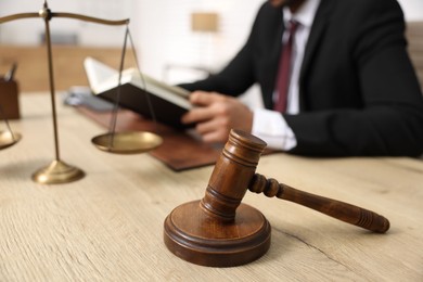 Lawyer reading book at table in office, focus on gavel