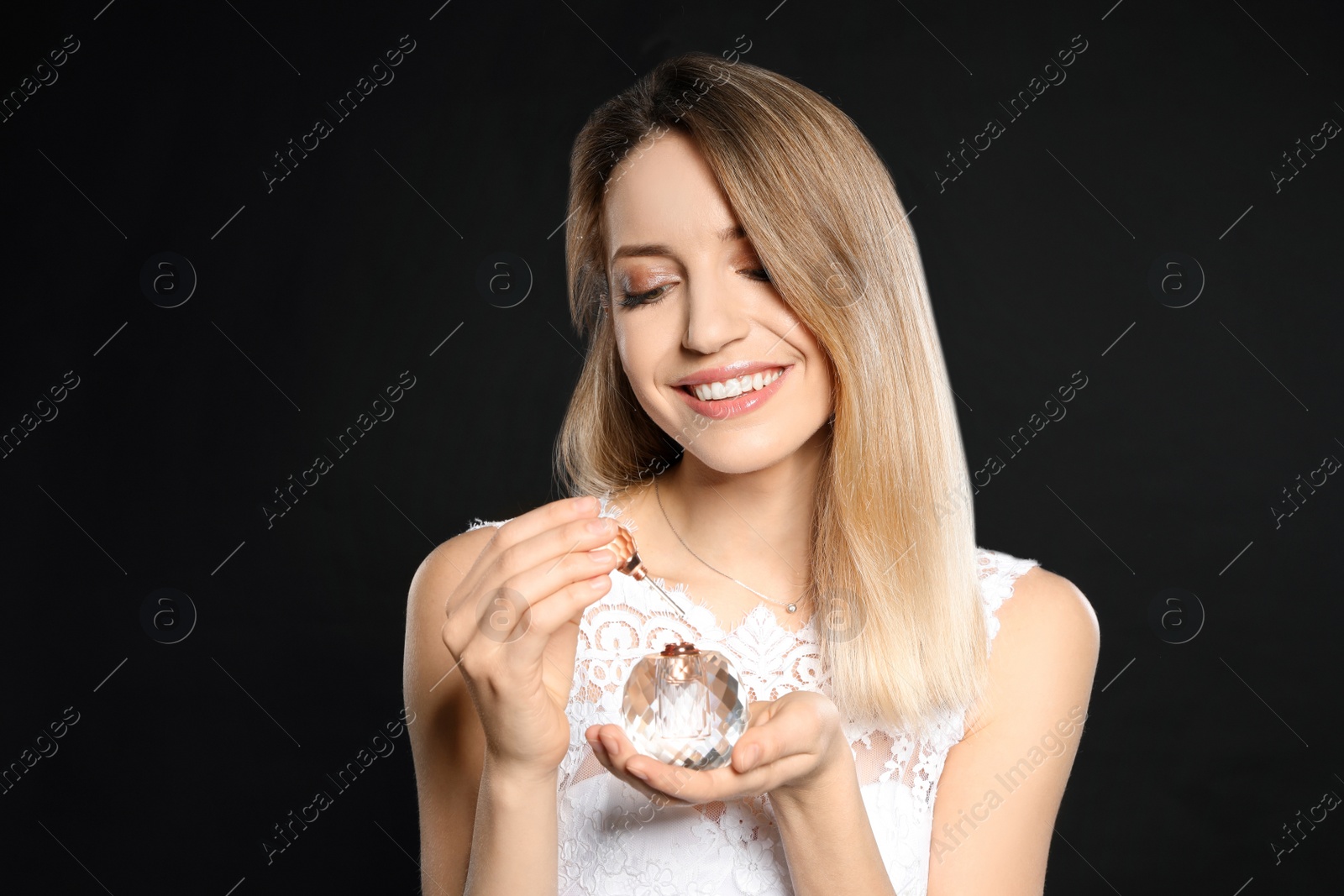 Photo of Beautiful young bride applying perfume against black background