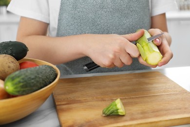 Photo of Woman peeling fresh zucchini with knife at white marble table in kitchen, closeup