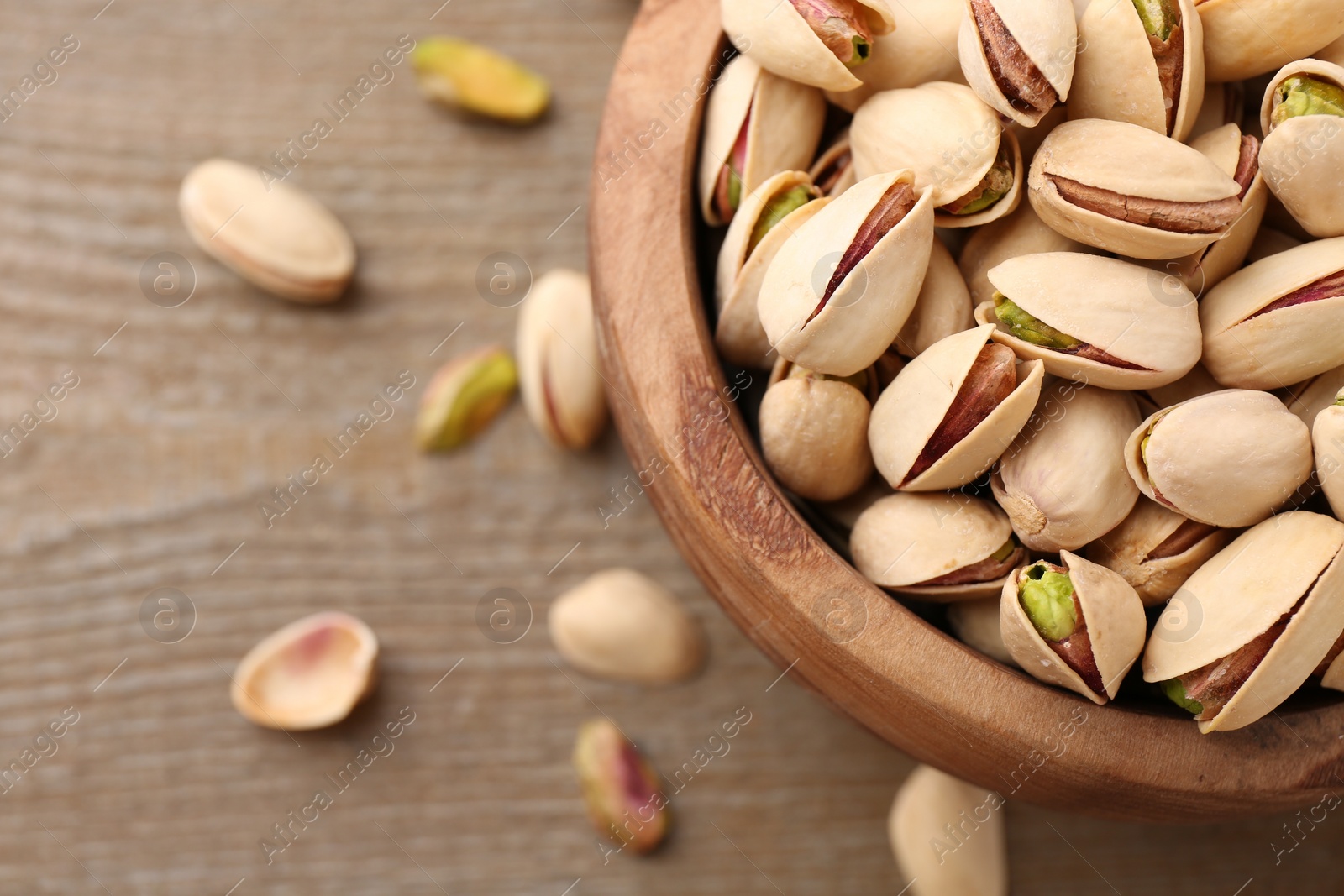 Photo of Tasty pistachios in bowl on wooden table, top view. Space for text