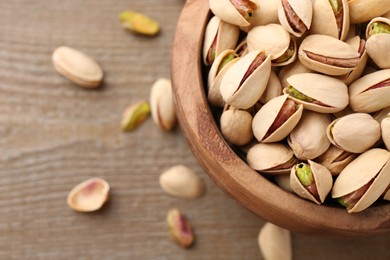 Tasty pistachios in bowl on wooden table, top view. Space for text