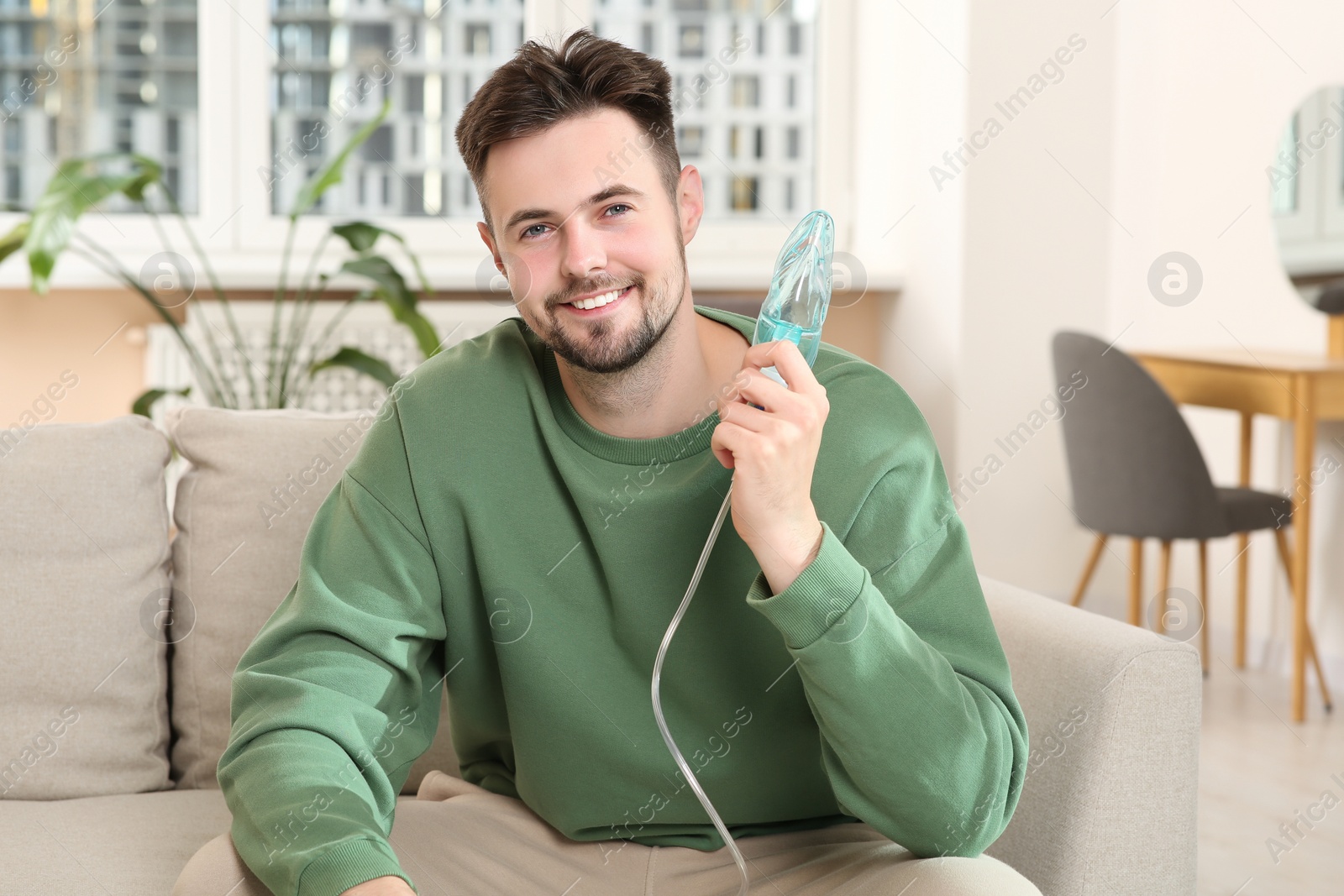 Photo of Smiling man holding nebulizer for inhalation on sofa at home