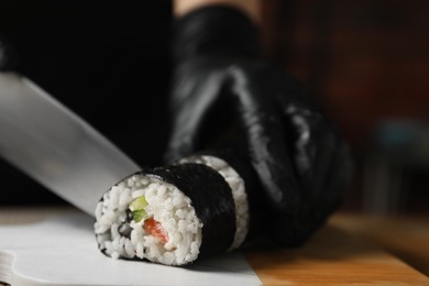 Chef in gloves cutting sushi roll at table, closeup