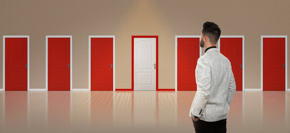 Image of Young man standing in front of many doors. Choice concept