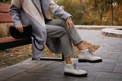 Photo of Stylish woman with trendy black baguette bag on bench in park, closeup