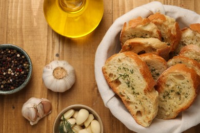 Tasty baguette with garlic, oil and other spices on wooden table, flat lay