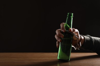 Photo of Alcohol addiction. Man handcuffed to bottle of beer at wooden table, closeup. Space for text