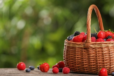 Photo of Wicker basket with different fresh ripe berries on wooden table outdoors, space for text