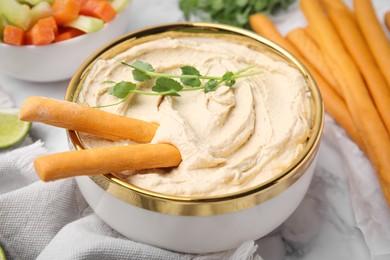 Photo of Delicious hummus with grissini sticks served on white marble table, closeup