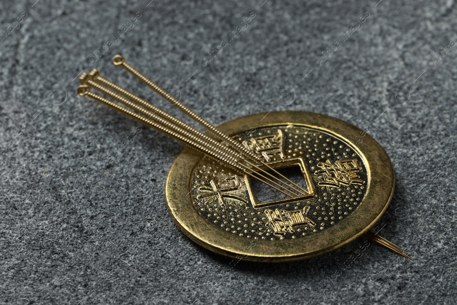 Photo of Acupuncture needles and ancient coin on grey textured table, closeup