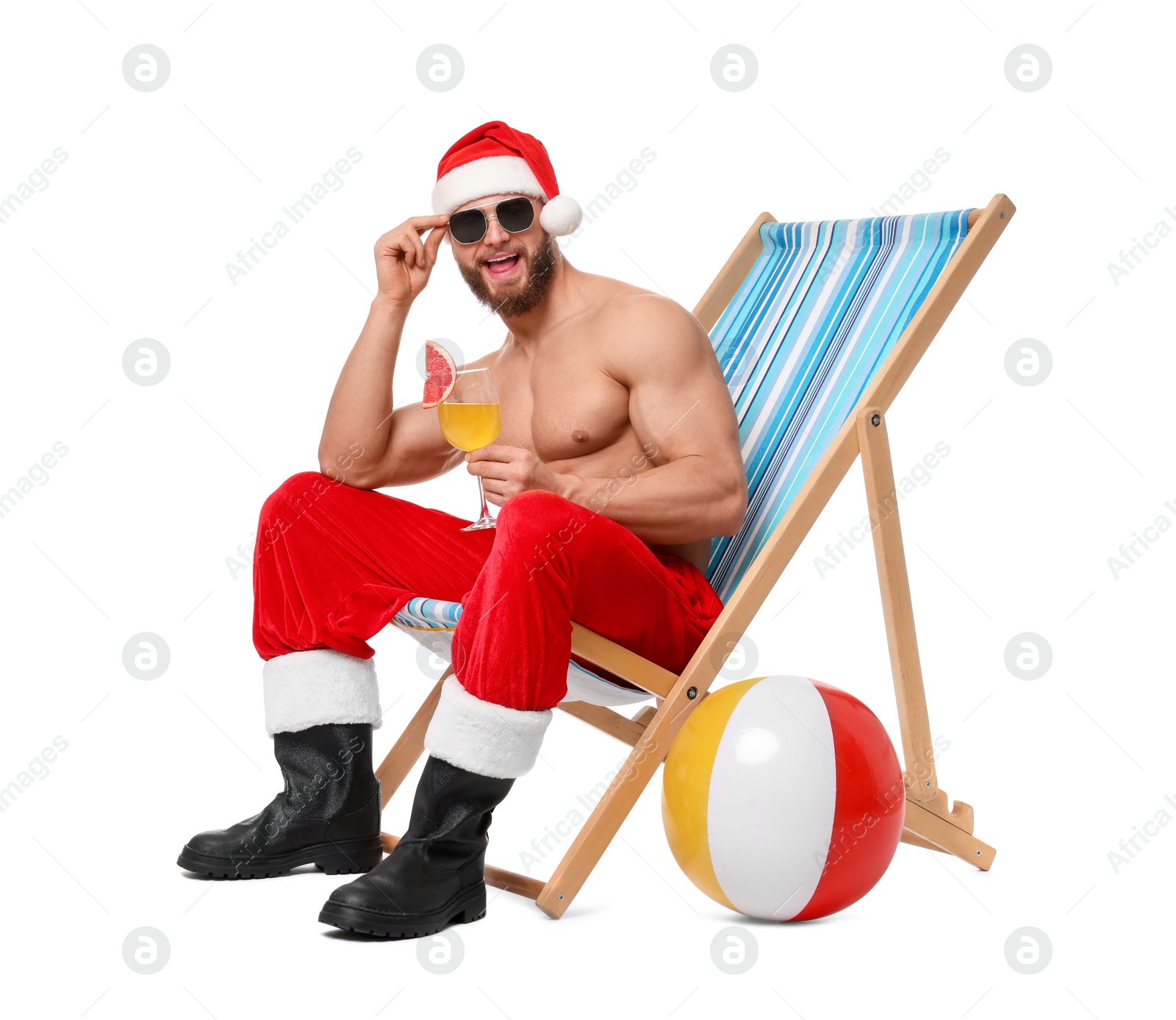 Photo of Muscular young man in Santa hat with deck chair, ball, sunglasses and cocktail on white background