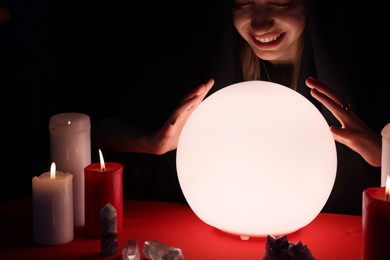 Photo of Soothsayer using glowing crystal ball to predict future at table in darkness. Fortune telling