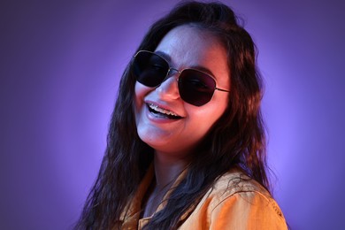 Portrait of beautiful young woman with stylish sunglasses on color background with neon lights