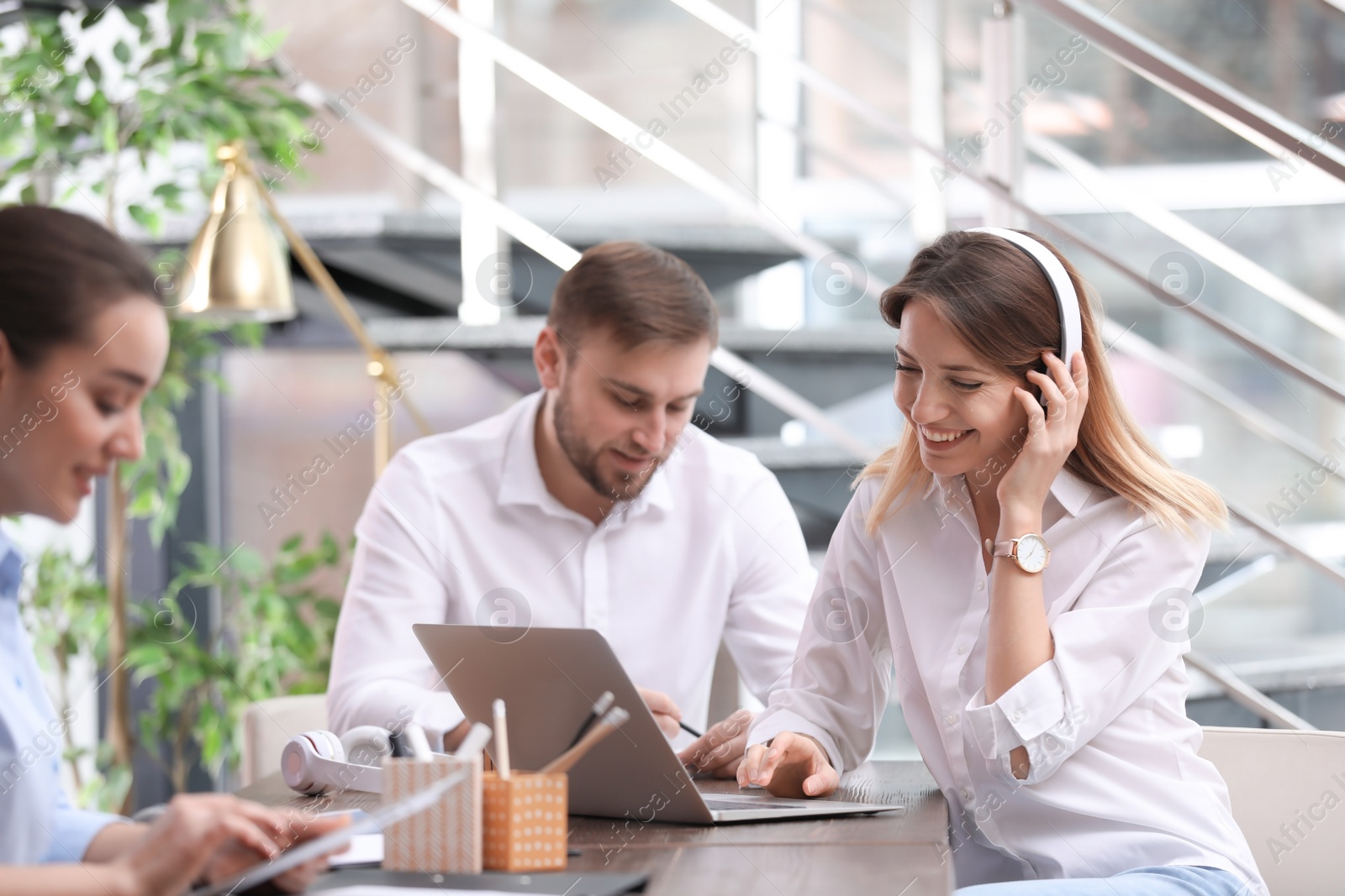 Photo of Young businesswoman with headphones, laptop and her colleagues working in office