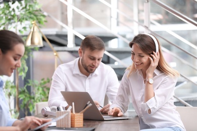 Photo of Young businesswoman with headphones, laptop and her colleagues working in office