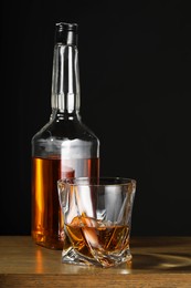 Photo of Whiskey in glass and bottle on wooden table against black background
