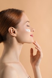 Beautiful young woman with sun protection cream on her face against beige background