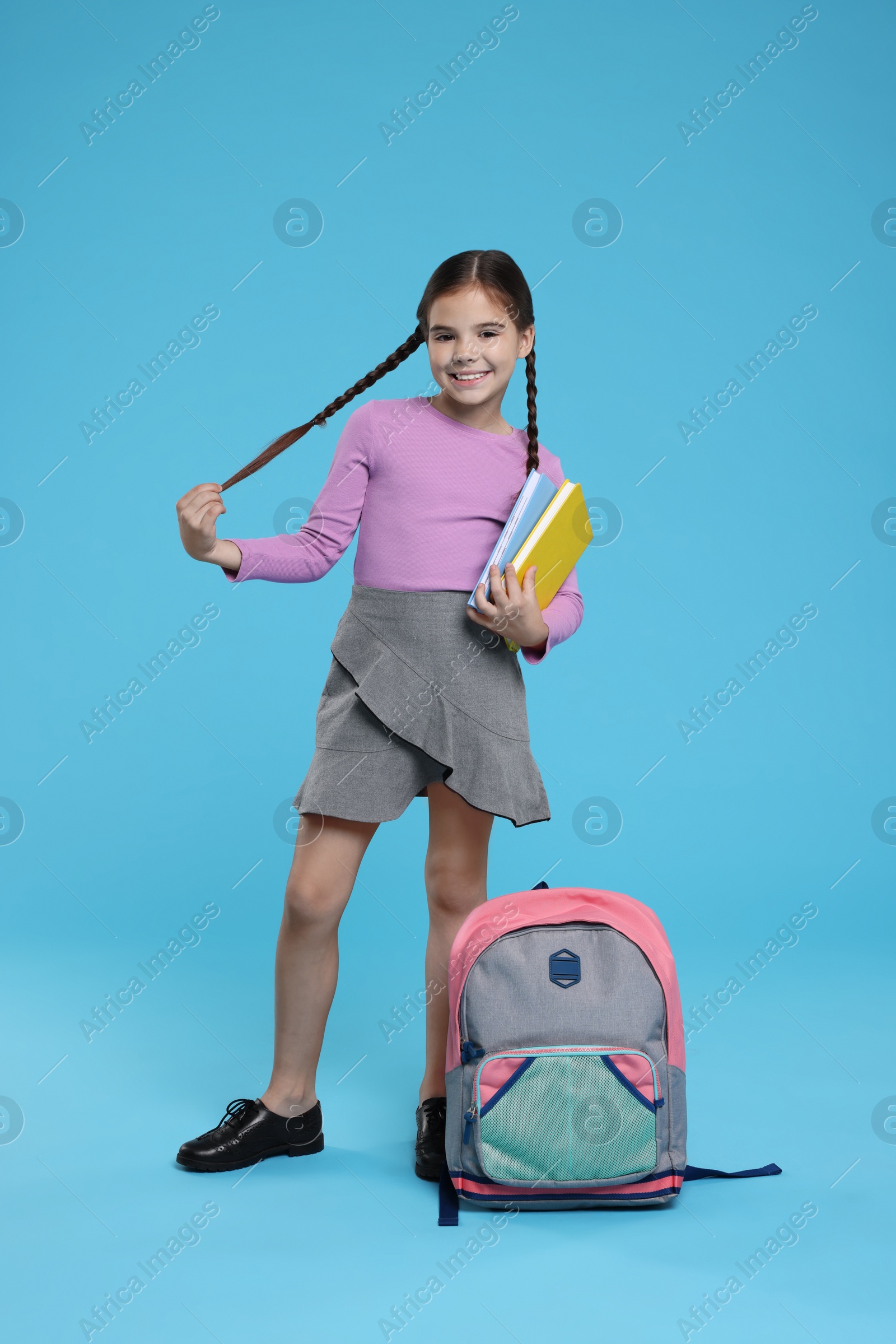 Photo of Cute schoolgirl with books on light blue background