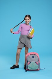 Cute schoolgirl with books on light blue background