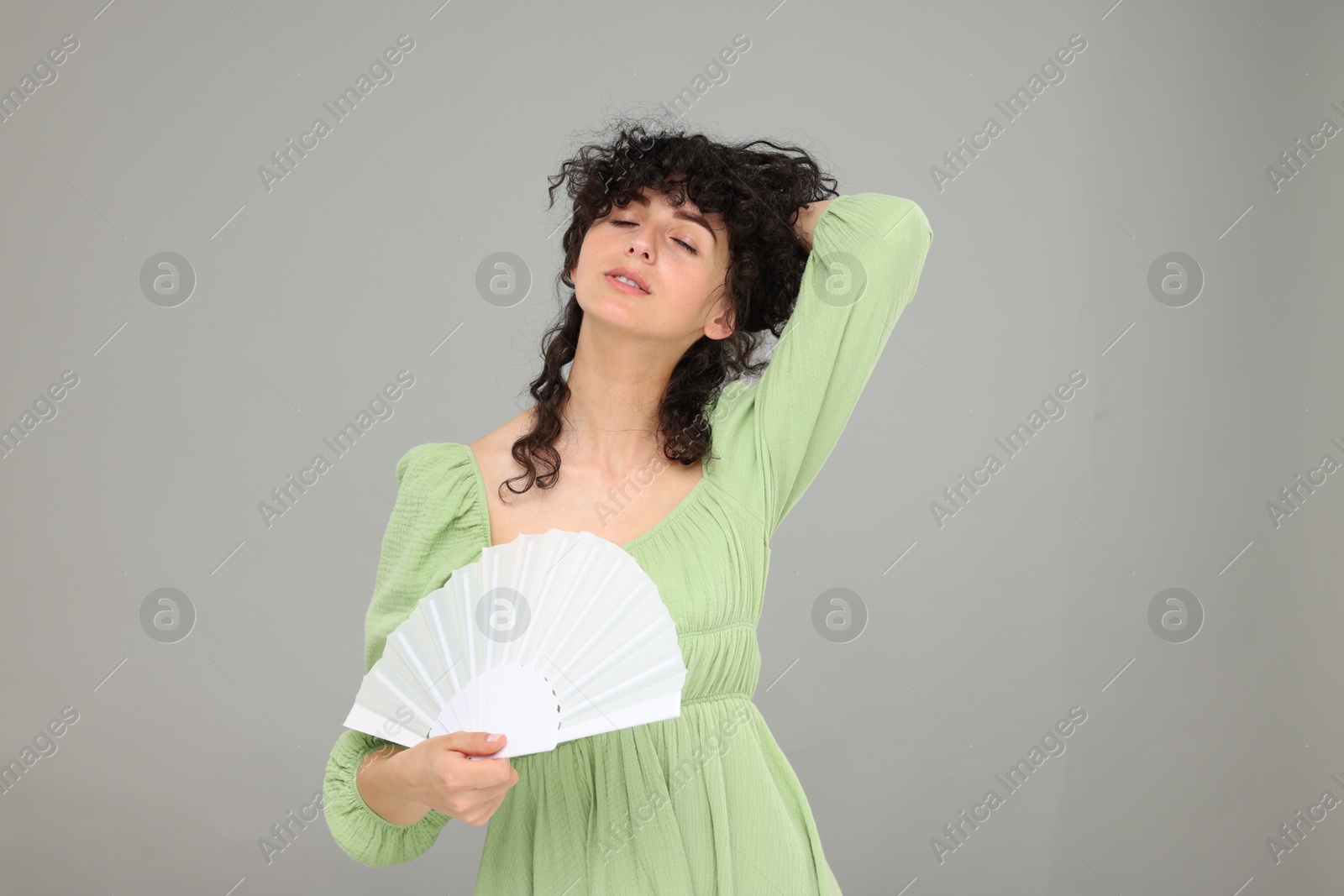 Photo of Woman with hand fan suffering from heat on light grey background