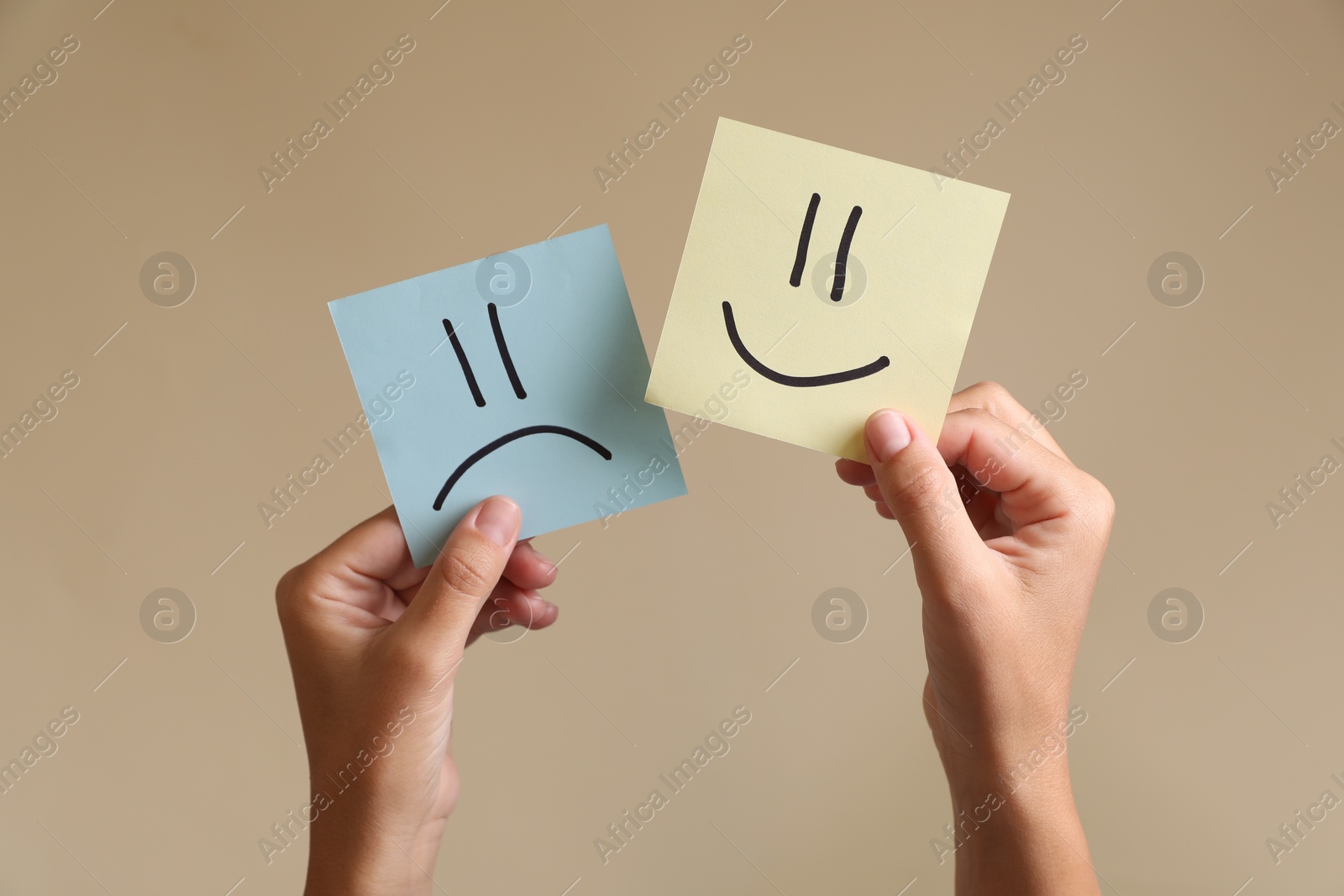 Photo of Choice concept. Woman holding papers with sad and happy emoticons on beige background, closeup