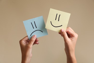 Photo of Choice concept. Woman holding papers with sad and happy emoticons on beige background, closeup